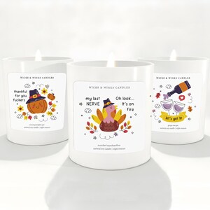 May include: Three white candles with humorous labels. One candle has a pumpkin wearing a witch hat, another has a turkey, and the last has wine glasses. The labels read "thankful for you fuckers", "my last NERVE, It's on fire", and "let's get it".