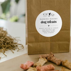 May include: A brown paper bag with a white circular sticker that says "Barking Bakery dog treats" with three dog paw prints below the text. The sticker also says "Peanut Butter & Carrot" and lists the ingredients: whole wheat flour, eggs, peanut butter, carrots, honey, cornstarch.