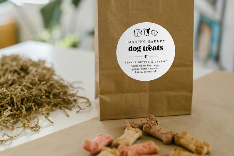 May include: A brown paper bag with a white circular sticker that says "Barking Bakery dog treats" with three dog paw prints below the text. The sticker also says "Peanut Butter & Carrot" and lists the ingredients: whole wheat flour, eggs, peanut butter, carrots, honey, cornstarch.