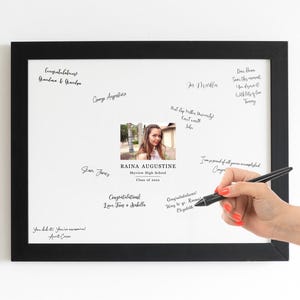 May include: A white framed board with a black border, featuring a photo of a young woman and handwritten messages. The text includes "Congratulations Raina Augustine, Skyview High School, Class of 2024".