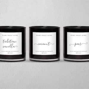 Puede incluir: Tres tarros de velas de vidrio negro con etiquetas blancas. Las etiquetas dicen "Home Sweet Home" y los aromas de las velas son "Vainilla de Tahití", "Coco" y "Pera".