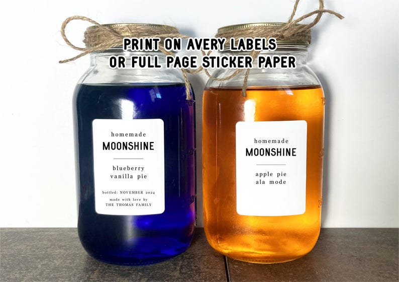 May include: Two glass jars with labels that say "homemade moonshine". The jar on the left is filled with a blue liquid and the label says "blueberry vanilla pie". The jar on the right is filled with a yellow liquid and the label says "apple pie ala mode".