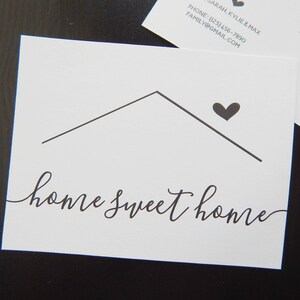 May include: A white card with a black house outline and a black heart above it. The text "home sweet home" is written in black cursive script.