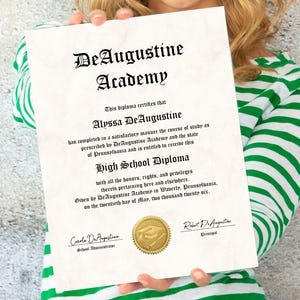 May include: A high school diploma from DeAugustine Academy, with the name Alyssa DeAugustine. The diploma is on aged paper with a gold seal and black text. The person holding the diploma is wearing a green and white striped shirt.