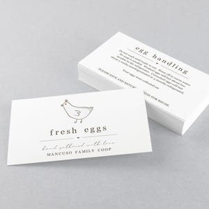 Può includere: Biglietti bianchi con testo nero e un'illustrazione di pollo dei cartoni animati. Un biglietto recita "fresh eggs" e "hand gathered with love". Un altro biglietto ha le istruzioni per la "egg handling". I biglietti sono di Mancuso Family Coop.