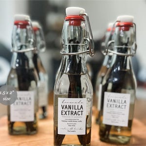 May include: Clear glass bottles with swing-top lids and red rubber seals, each containing dark vanilla beans submerged in liquid. A white rectangular label measuring 3.81 x 5.08 cm reads Homemade VANILLA EXTRACT, INGREDIENTS Tahitian vanilla beans, vodka, BOTTLED July 2024, made with love by The Loack's.