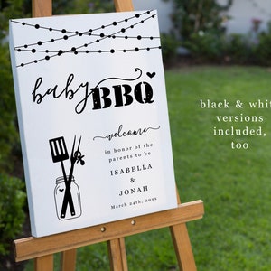 May include: A white sign with black text and graphics announcing a "baby BBQ" in honor of the parents to be, Isabella and Jonah. The sign features a string of lights, a jar with a spatula and tongs, and the date March 24th, 20xx.