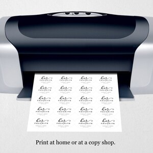 Op de afbeelding: Een zwart-zilveren printer met een vel papier dat eruit komt. Het papier heeft meerdere labels erop gedrukt die "haar favoriet" zeggen in een cursief schrift.