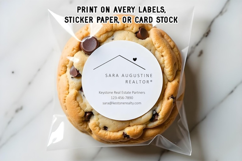 Pu&ograve; includere: Un grande biscotto con gocce di cioccolato in un sacchetto di cellophane trasparente. Il biscotto ha un'etichetta bianca con il testo "SARA AUGUSTINE REALTOR&reg;" e le informazioni di contatto. Il testo in alto recita "PRINT ON AVERY LABELS, STICKER PAPER, OR CARD STOCK."