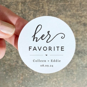 Op de afbeelding: Ronde witte sticker met zwarte tekst die "her favorite" zegt met een klein hartje en de namen "Colleen + Eddie" en de datum "08.09.24".