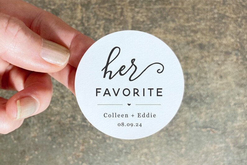 Op de afbeelding: Ronde witte sticker met zwarte tekst die "her favorite" zegt met een klein hartje en de namen "Colleen + Eddie" en de datum "08.09.24".