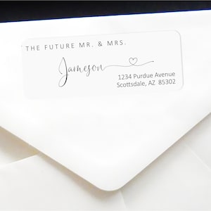 Può includere: Busta bianca con un'etichetta trasparente che dice "THE FUTURE MR. & MRS. Jameson" con un cuore e l'indirizzo "1234 Purdue Avenue Scottsdale, AZ 85302".