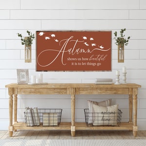 May include: A rustic wooden console table with two black wire baskets, a white pillow with the text "welcome home", and a framed sign with the text "Autumn shows us how beautiful it is to let things go" on a white shiplap wall.