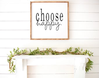 May include: A white wooden sign with the text "choose happy" in black lettering. The sign is hanging on a white wood wall above a white mantel with a green garland.