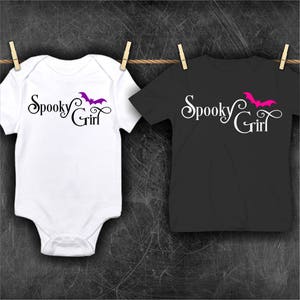 May include: Two white t-shirts with the text "Spooky Girl" and a bat graphic. One shirt has a purple bat and the other has a pink bat.