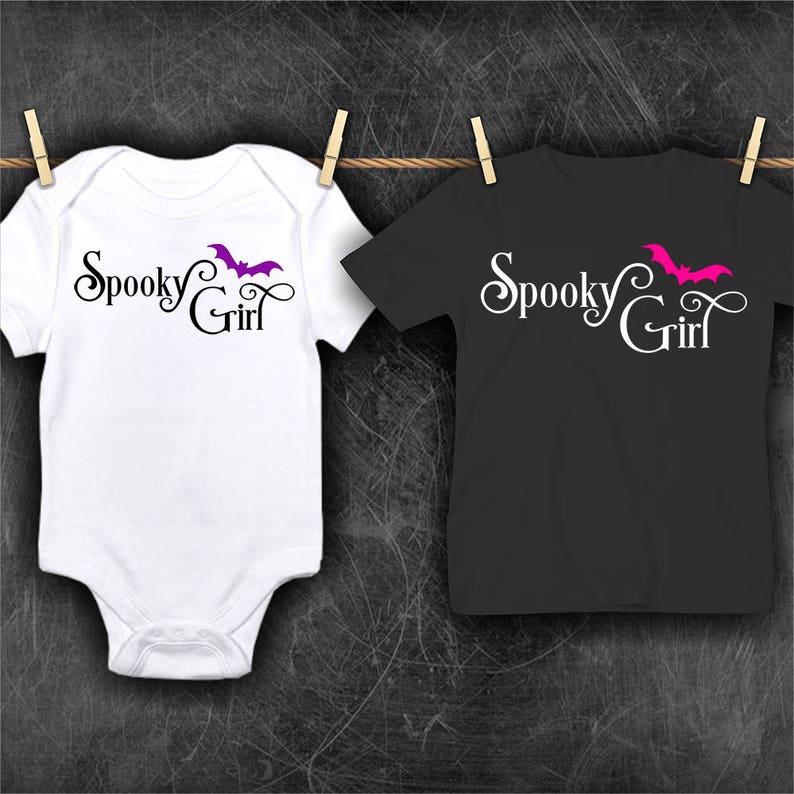 May include: Two white t-shirts with the text "Spooky Girl" and a bat graphic. One shirt has a purple bat and the other has a pink bat.