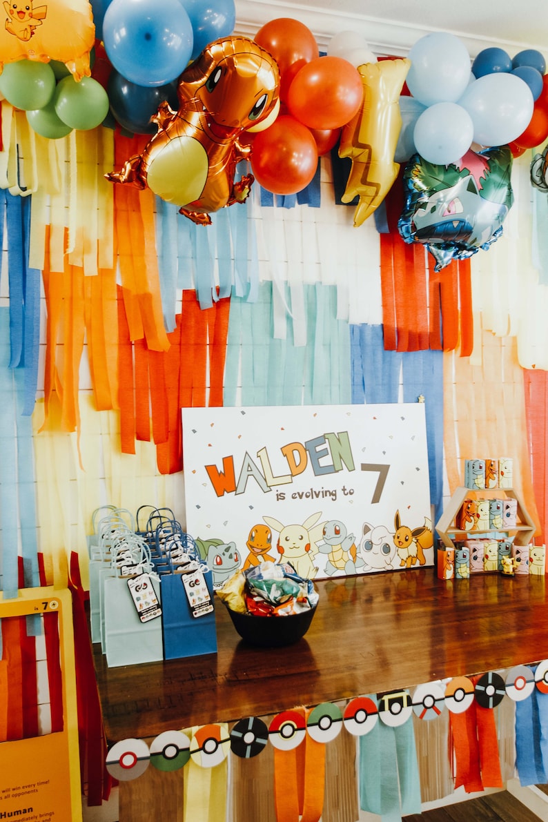 May include: A Pokemon-themed birthday party decoration with a sign that says "Walden is evolving to 7". The sign is surrounded by colourful balloons and streamers. There are also small Pokemon figurines and gift bags.