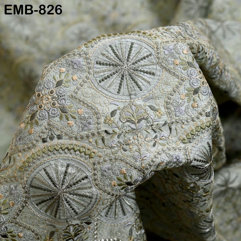 May include: Close-up of intricately embroidered fabric in shades of pale green, silver, and gold. The design features repeating circular patterns with radial lines and floral motifs. The text "EMB-826" is visible in the upper left corner.