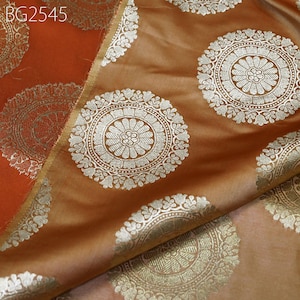 Puede incluir: Primer plano de una tela con un patrón repetitivo de círculos dorados y plateados. La tela es de color marrón claro y los círculos tienen un diseño blanco.