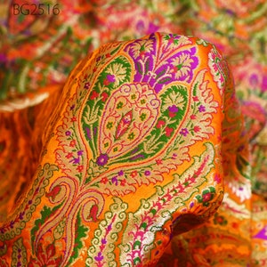 Op de afbeelding: Oranje stof met een paisley-patroon in groen, roze, paars en goud. De stof is geweven met een reli&euml;fstructuur.