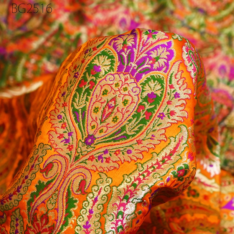 Op de afbeelding: Oranje stof met een paisley-patroon in groen, roze, paars en goud. De stof is geweven met een reli&euml;fstructuur.