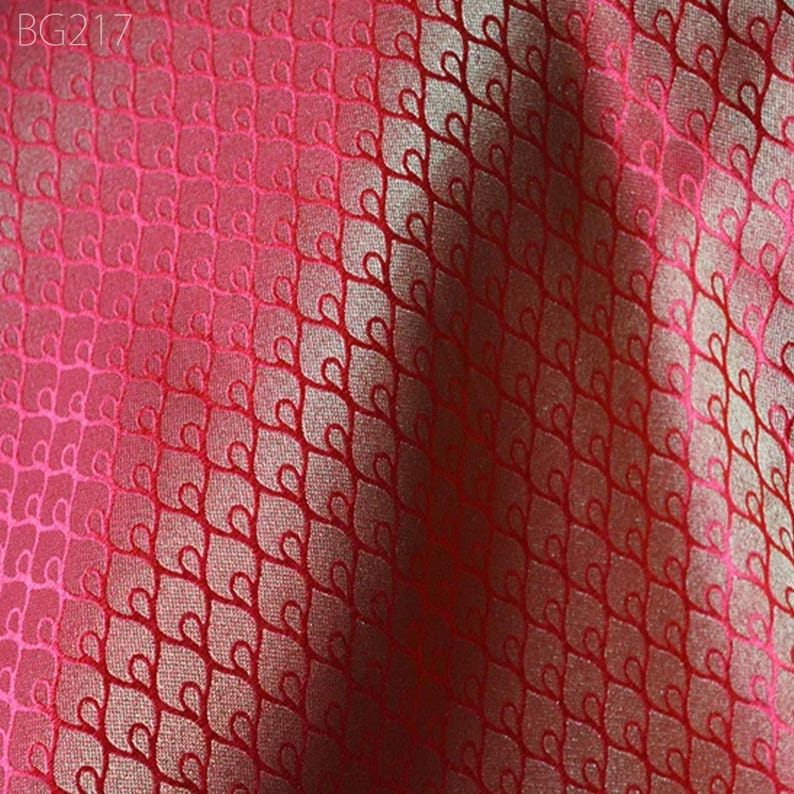 May include: Red fabric with a repeating pattern of small, stylised hearts. The fabric has a subtle sheen and a slightly textured surface.