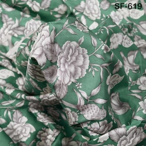 Pode incluir: Tecido verde com um padrão floral de grandes flores cinzentas e brancas, folhas e pássaros. O tecido tem um brilho acetinado e está dobrado, mostrando o design detalhado. O texto "SF-619" está no canto superior direito.