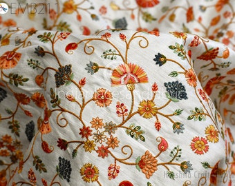 Puede incluir: Tela blanca con un patrón de bordado floral en tonos de naranja, amarillo, verde y azul. El bordado presenta flores y enredaderas delicadas.