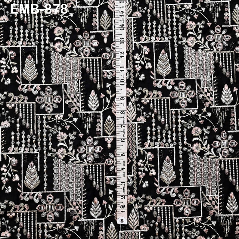 May include: Black fabric featuring an embroidered floral design in white, silver, and pale pink. The pattern includes geometric shapes, floral motifs, and vertical beaded lines. The text "EMB.878" is visible in the upper left corner.