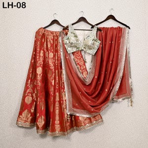 Peut inclure: Ensemble de vêtements ethniques indiens en trois pièces. L'ensemble comprend une jupe rouge avec des motifs floraux dorés, un haut argenté et doré orné et un châle rouge avec une bordure argentée. La tenue est présentée sur des cintres.