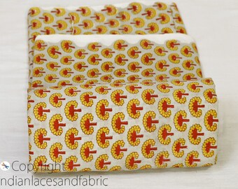 May include: A roll of fabric with a white background and a repeating pattern of yellow and red trees. The fabric is folded in thirds and the edges are slightly frayed.