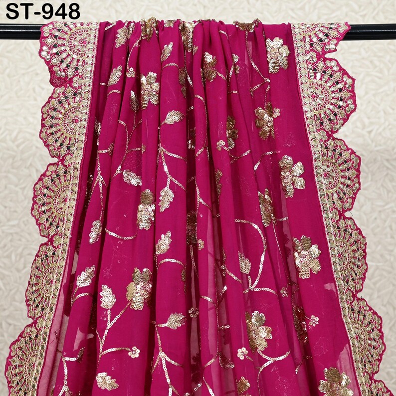Puede incluir: Una vibrante tela fucsia con bordados florales dorados y detalles de lentejuelas. El borde presenta un ribete dorado festoneado con intrincados detalles de espejo. La tela est&aacute; drapeada, mostrando su textura fluida. El texto "ST-948" es visible.