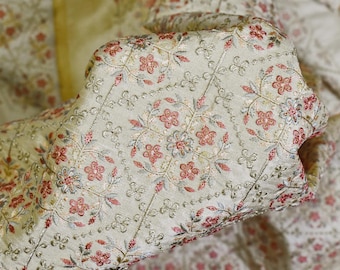 May include: A close-up of a light green fabric with a delicate floral pattern embroidered in shades of pink and gray. The fabric has a subtle sheen and a soft texture.