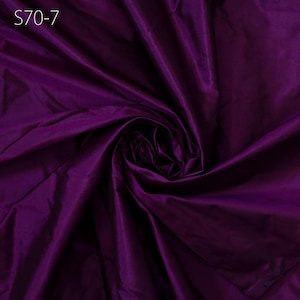 Pode incluir: Um close-up de um tecido roxo escuro com uma textura lisa e sedosa. O tecido está dobrado e drapeado, criando dobras e curvas suaves.