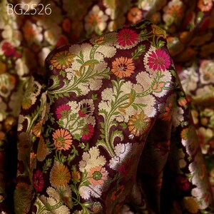 May include: A close-up of a brown fabric with a floral pattern. The fabric has a gold metallic thread woven into the design. The flowers are in shades of pink, orange, and green.