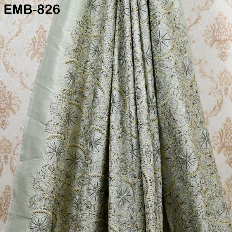 May include: A light green fabric with intricate embroidery featuring circular and floral patterns. The fabric is draped, showcasing the detailed design and texture. The text "EMB-826" is visible in the upper left corner.