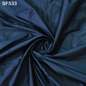 May include: A close-up of a deep blue fabric with a smooth, silky texture. The fabric is folded and draped, showcasing its luxurious feel.