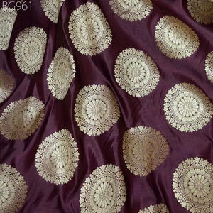 May include: Burgundy fabric with a repeating pattern of gold circular designs. The fabric has a subtle sheen and a soft texture.