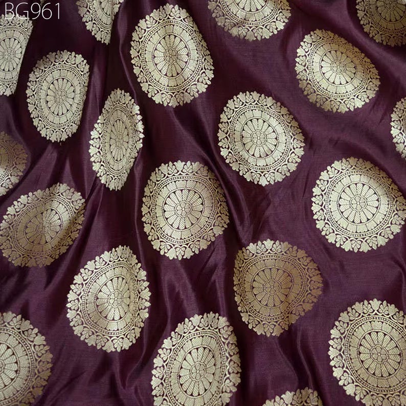 May include: Burgundy fabric with a repeating pattern of gold circular designs. The fabric has a subtle sheen and a soft texture.