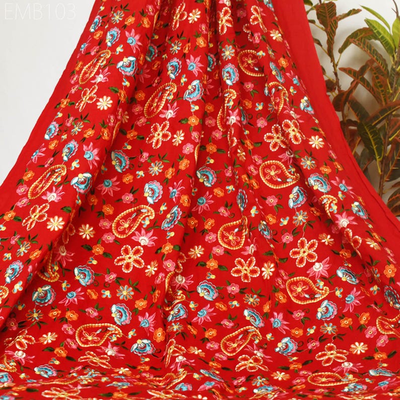 May include: Red fabric with a paisley and floral pattern. The fabric is embroidered with colorful thread and sequins.