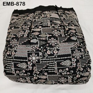 May include: Black fabric featuring an embroidered floral and geometric pattern with pink, white, and silver accents. The text "EMB-878" is visible. The fabric is folded, suggesting it is a textile, possibly for clothing or home decor.