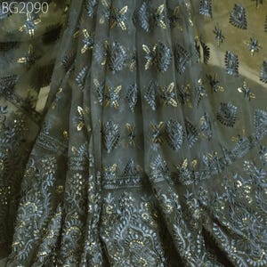 May include: A sheer fabric with a gray background and intricate embroidery in silver and gold. The fabric is decorated with a repeating pattern of geometric shapes and floral motifs.