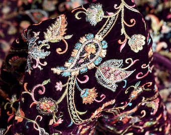 May include: Purple velvet fabric with intricate floral embroidery in shades of pink, orange, blue, and green. The fabric has a paisley pattern and is embellished with sequins.
