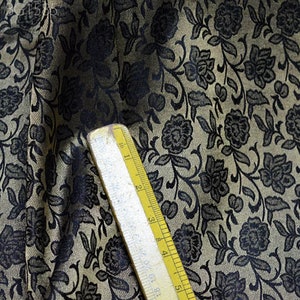 May include: Close-up of a fabric with a black floral pattern on a beige background. A ruler is visible in the bottom right corner.