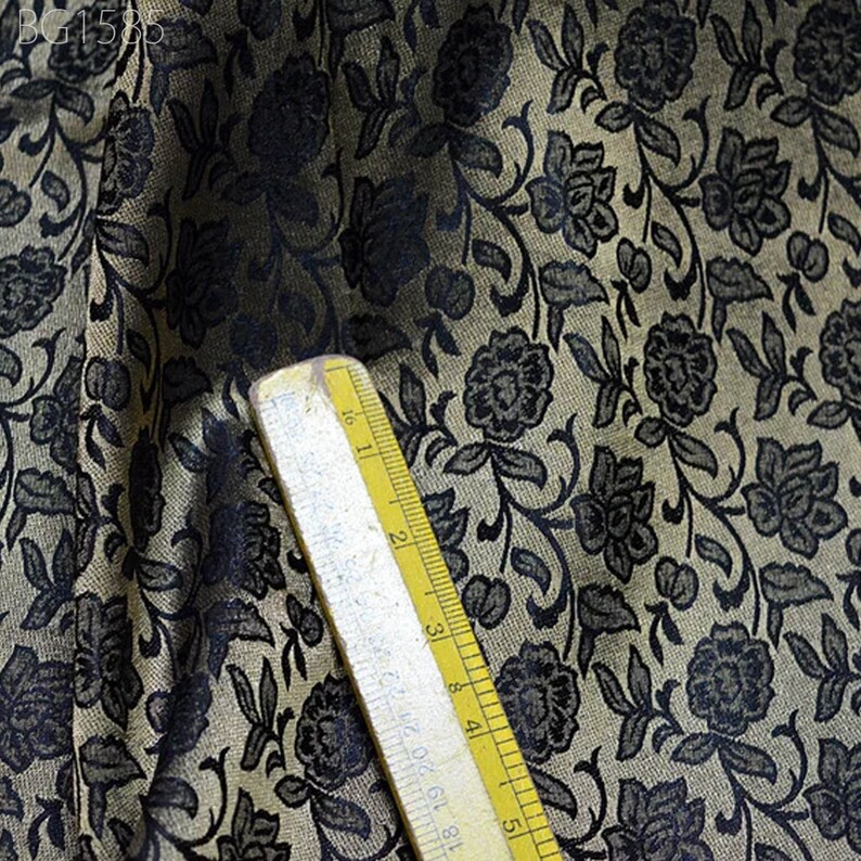 May include: Close-up of a fabric with a black floral pattern on a beige background. A ruler is visible in the bottom right corner.