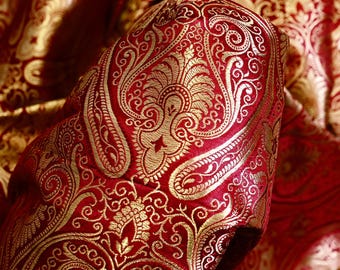 May include: Red fabric with a gold paisley pattern. The fabric is folded and the pattern is visible on both sides.