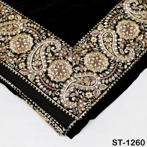 以下が含まれることがあります： 金、緑、クリーム色の複雑な刺繍が施された黒い織物。 デザインは、縁に沿って花柄とペイズリー柄が特徴です。 この織物はベルベットのような質感とスカラップのボーダーを持っています。