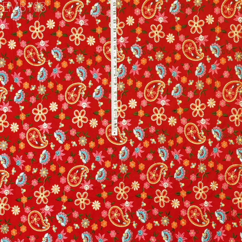 May include: Red fabric with a paisley and floral pattern. The fabric features a repeating pattern of small blue, pink, and orange flowers, along with paisley shapes in a light blue and white color scheme.
