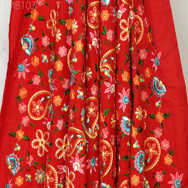 May include: Red fabric with intricate embroidery featuring paisley patterns and floral designs in shades of pink, blue, green, and orange. The fabric is embellished with gold thread and sequins.