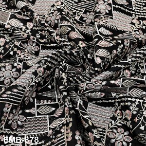 May include: Black fabric with detailed embroidery in white, pink, and beige, showcasing floral and geometric motifs. The fabric is draped, creating shadows. The text "BMB 878" is visible in the lower left corner of the image.